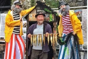 Stilt walkers and man holiding herrings at Clovelly Herring festival