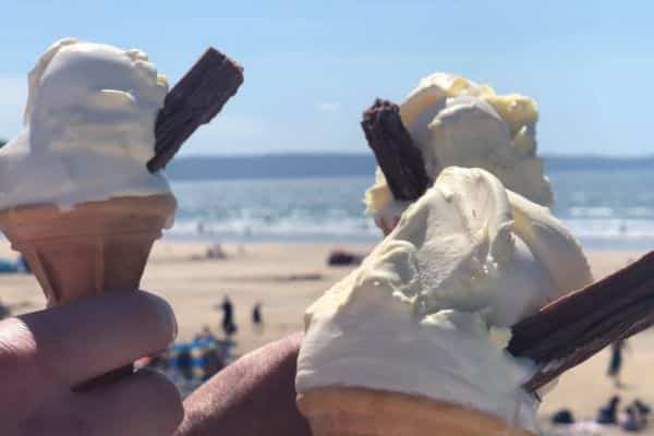 close up of peoples hands holiding Hockings ice creams with Westward Ho! beach in the background